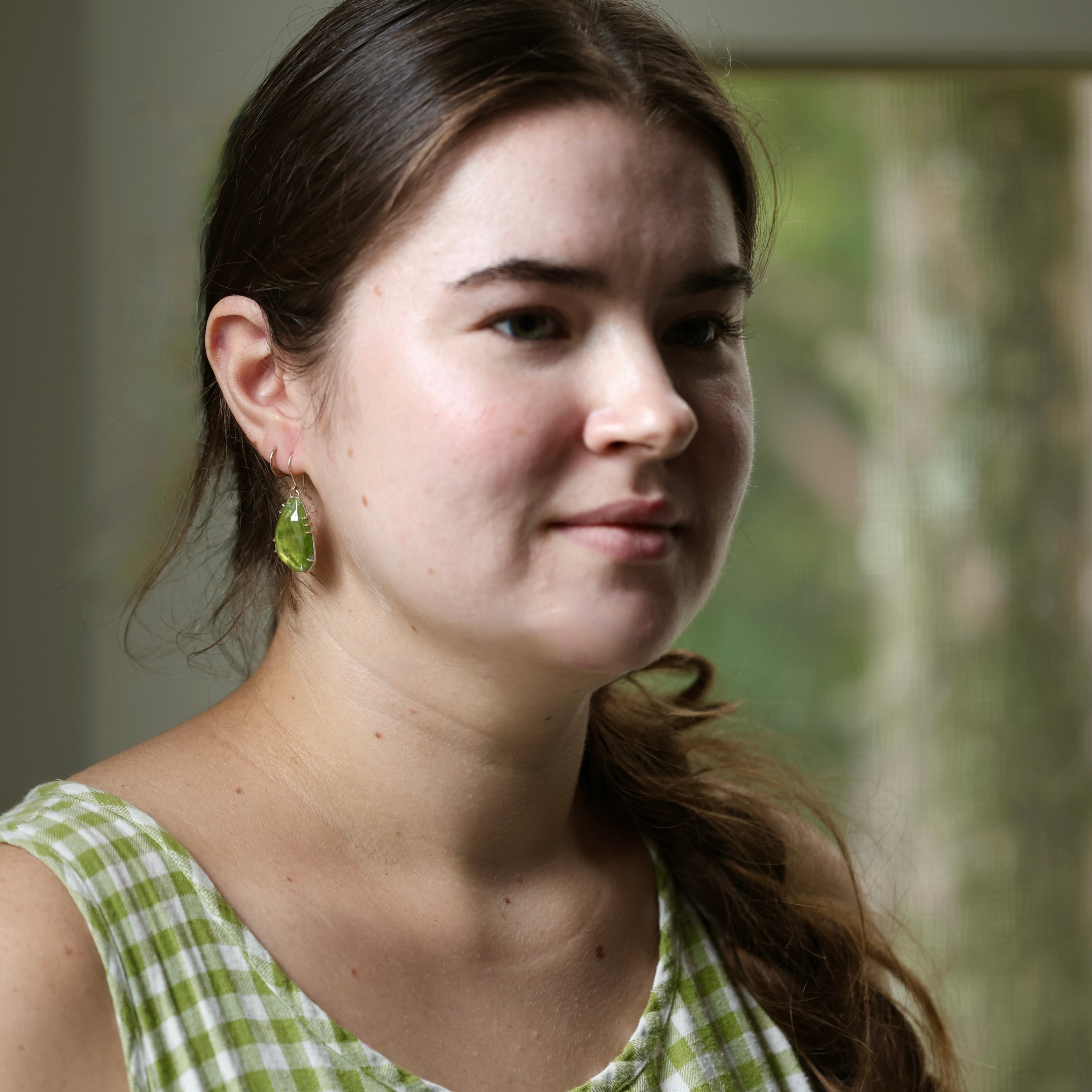 Woman wearing a green checkered dress  and green earrings with a blurred natural background