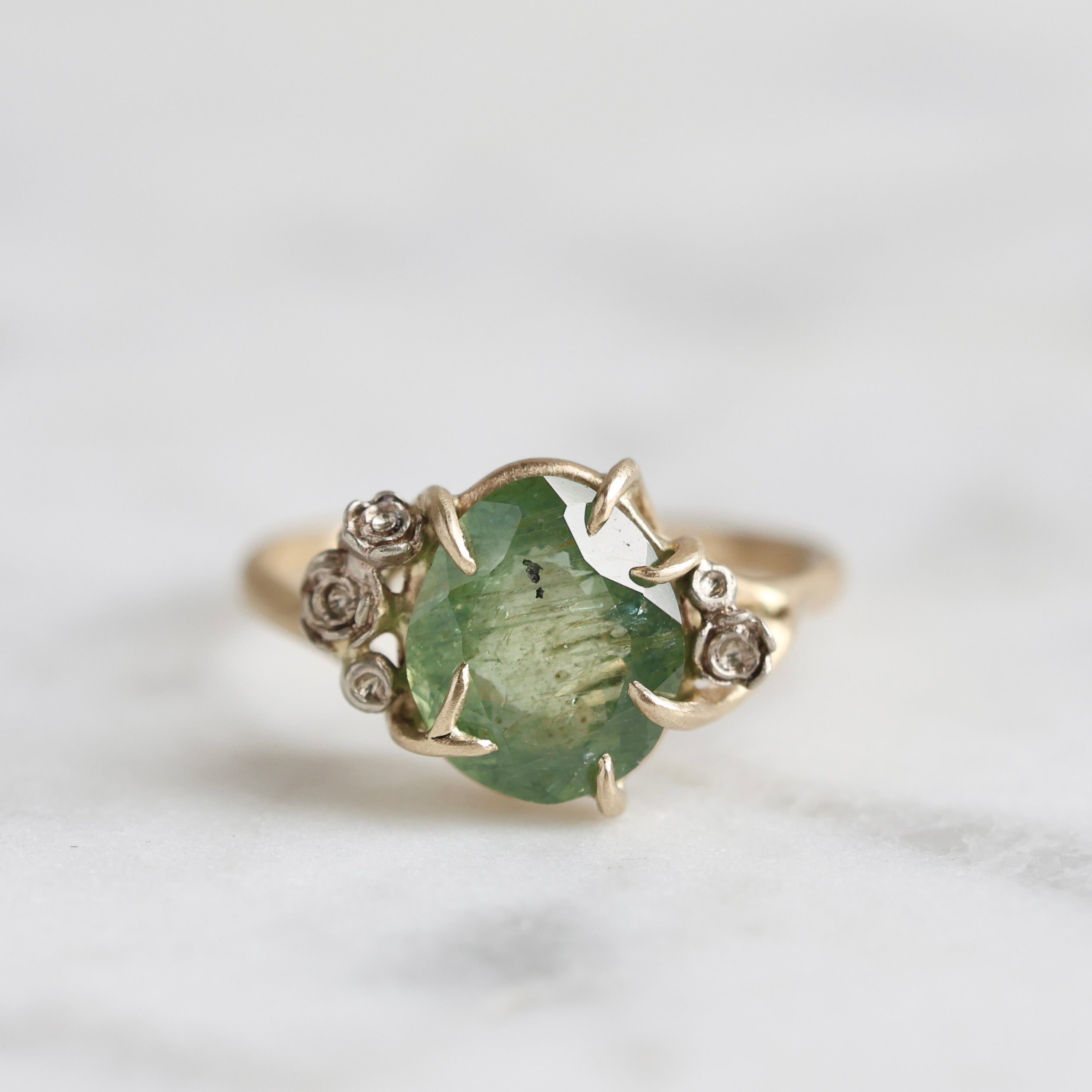 a green egg montana sapphire is in a ring of gold branches and white gold roses. 