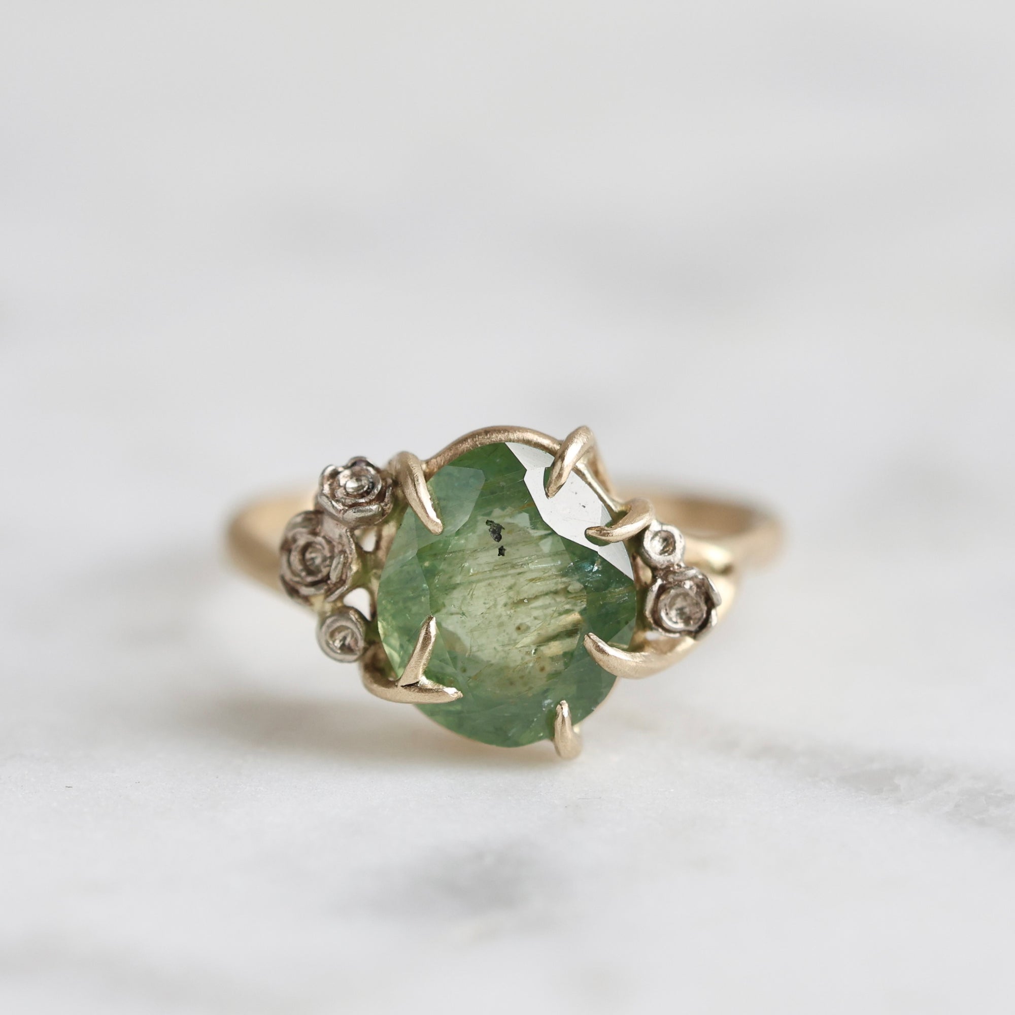 a green egg montana sapphire is in a ring of gold branches and white gold roses. 