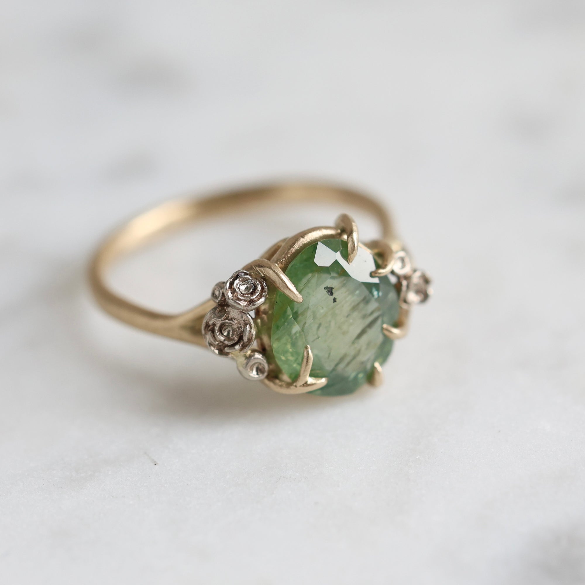 a green egg montana sapphire is in a ring of gold branches and white gold roses. 