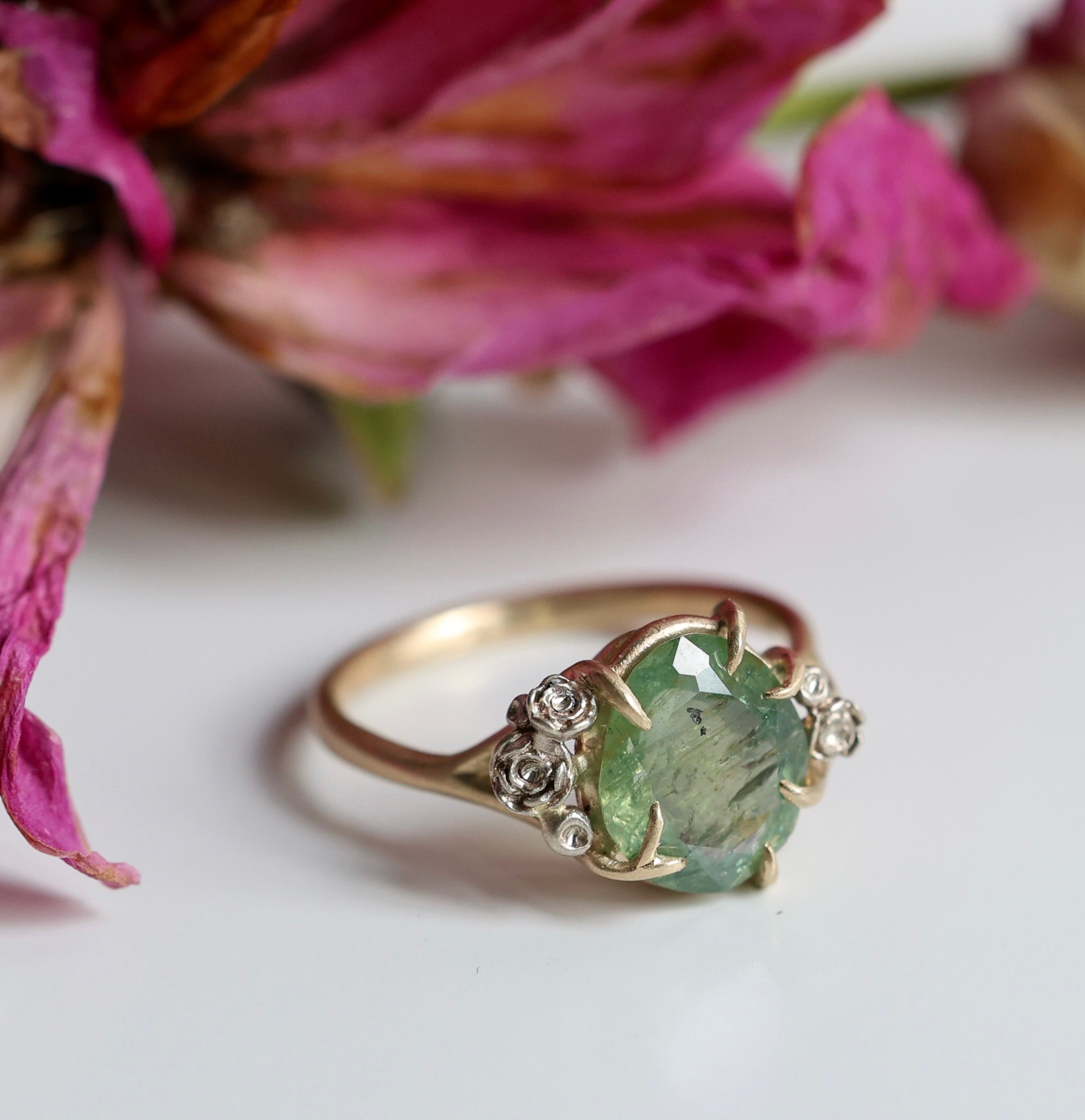 a green egg montana sapphire is in a ring of gold branches and white gold roses. photographed with decaying roses.