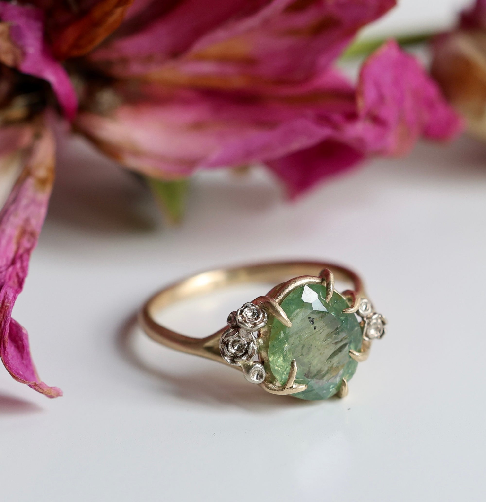 a green egg montana sapphire is in a ring of gold branches and white gold roses. photographed with decaying roses.