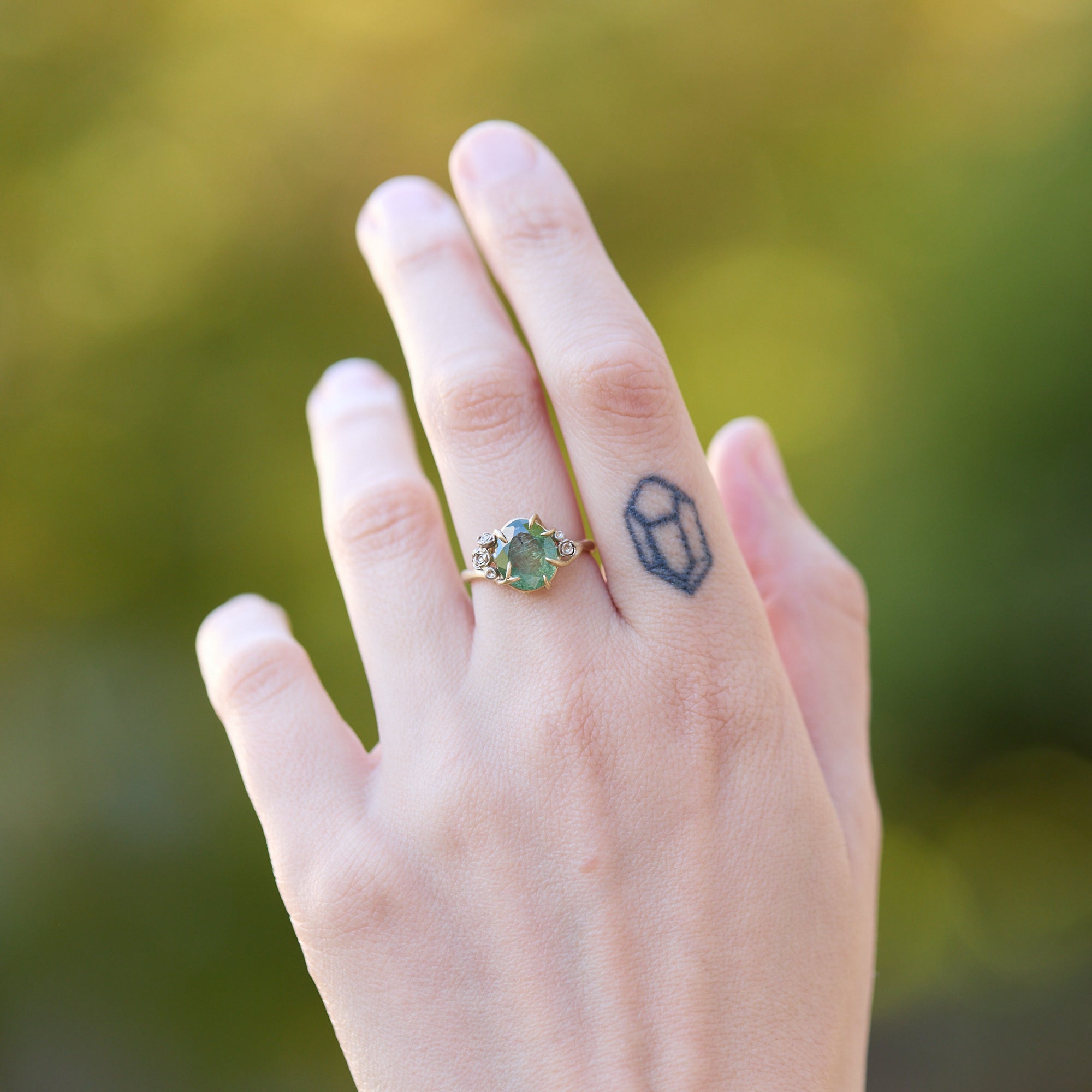 Hand wearing a ring with a green gemstone against a blurred green background