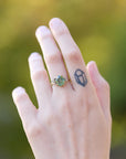 Hand wearing a ring with a green gemstone against a blurred green background