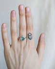 Hand wearing a ring with a blue gemstone on a plain background