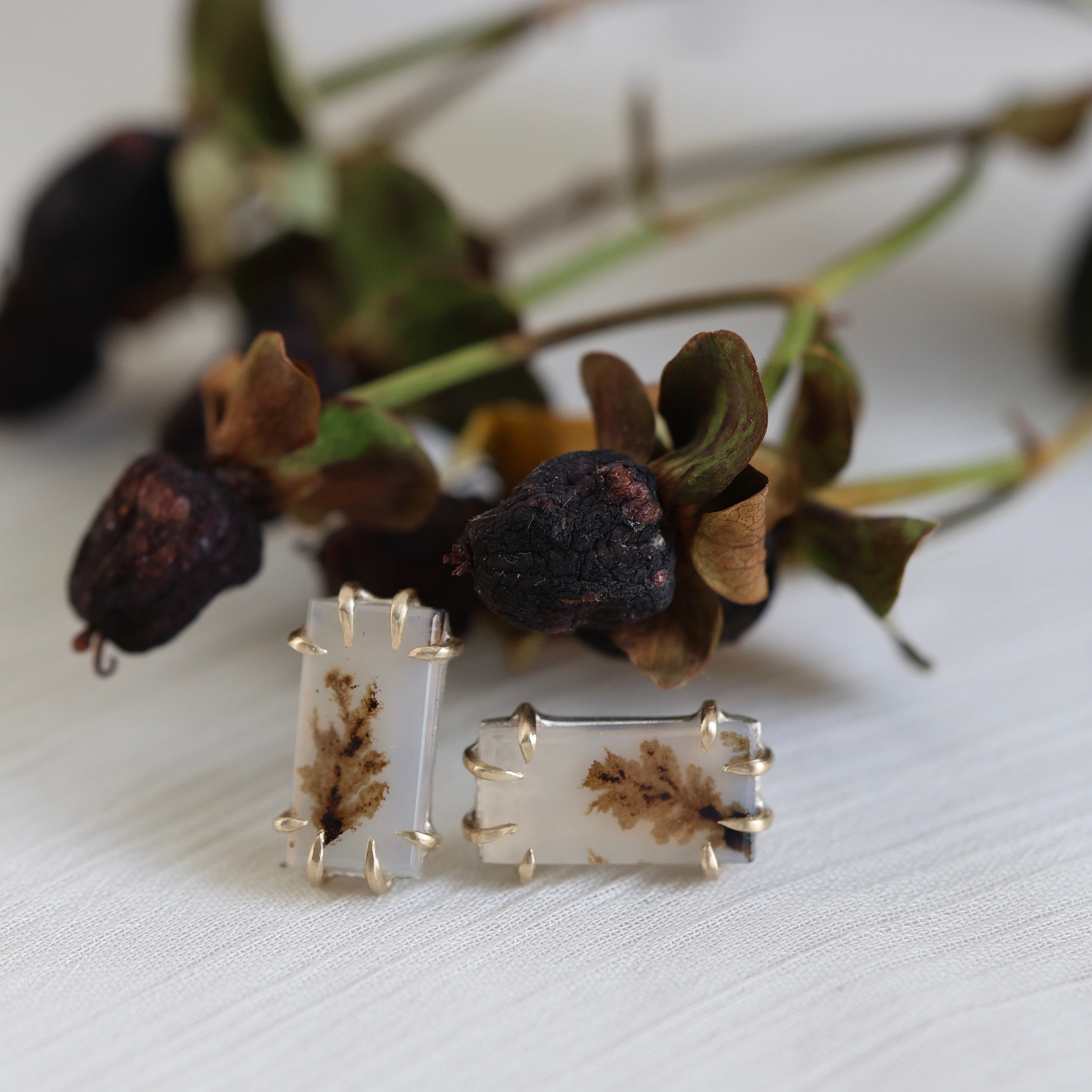 Pair of earrings with leaf design on a white surface with dried leaves in the background