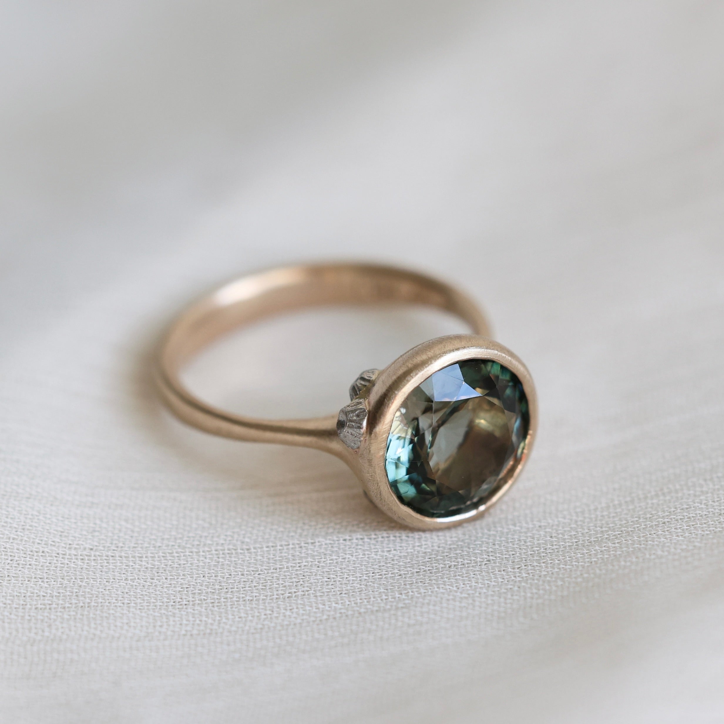 Gold ring with a green gemstone on a light fabric background