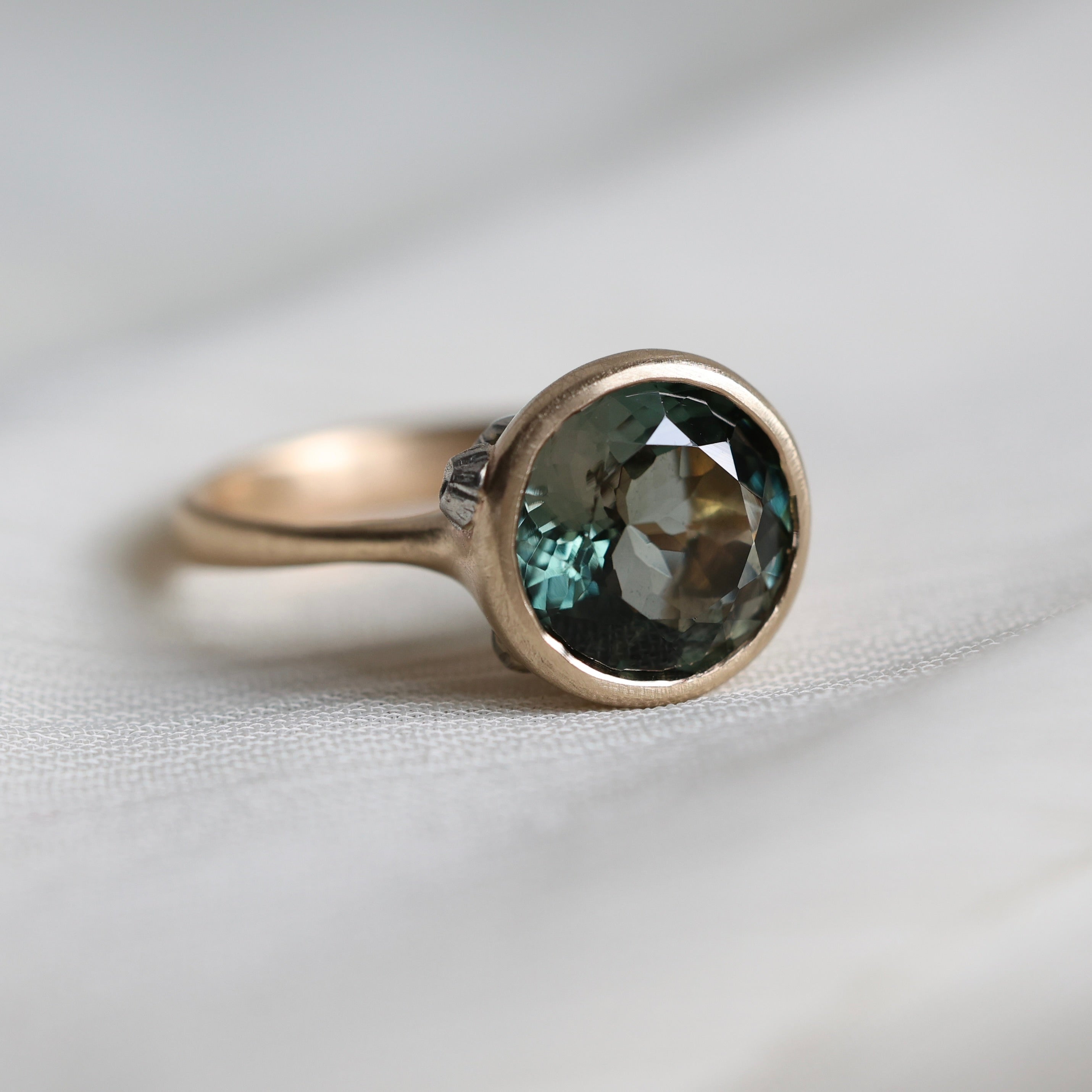Gold ring with a green gemstone on a light fabric background