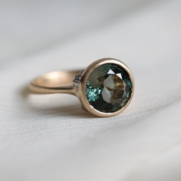 Gold ring with a green gemstone on a light fabric background
