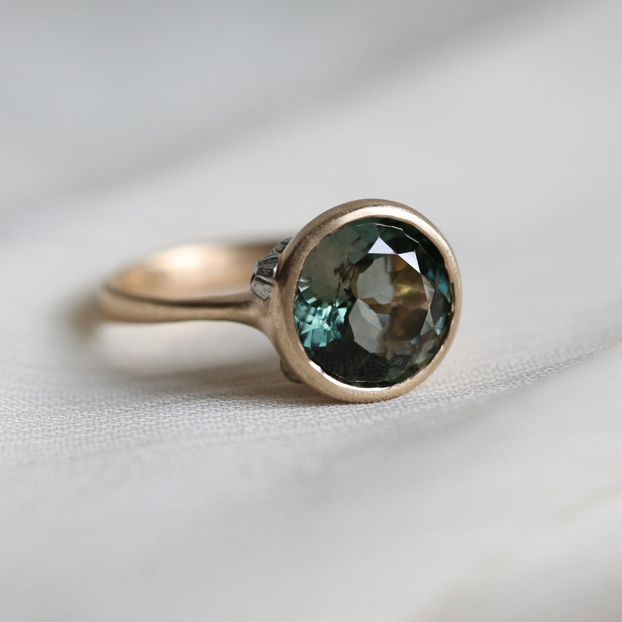 Gold ring with a green gemstone on a light fabric background