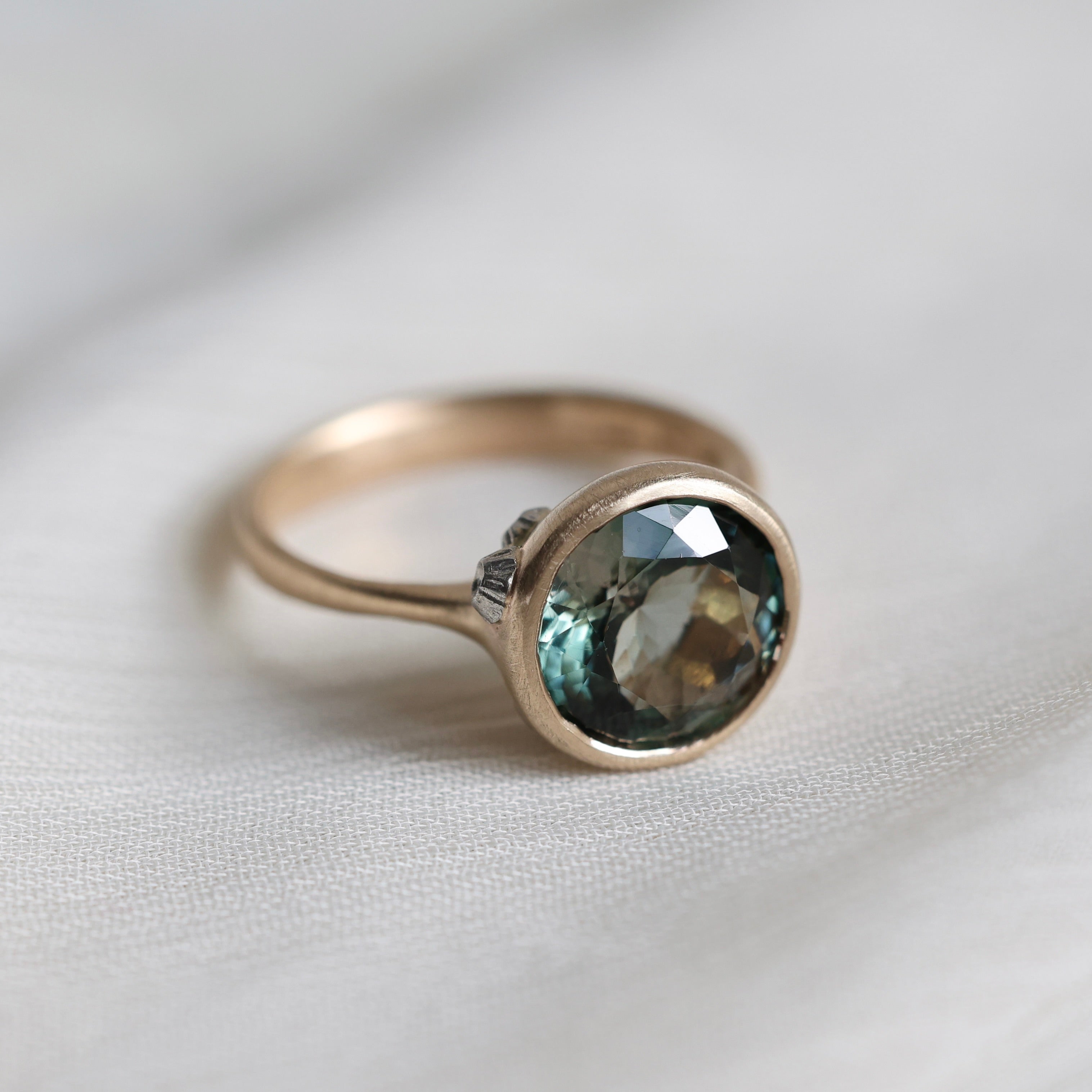 Gold ring with a green gemstone on a light fabric background