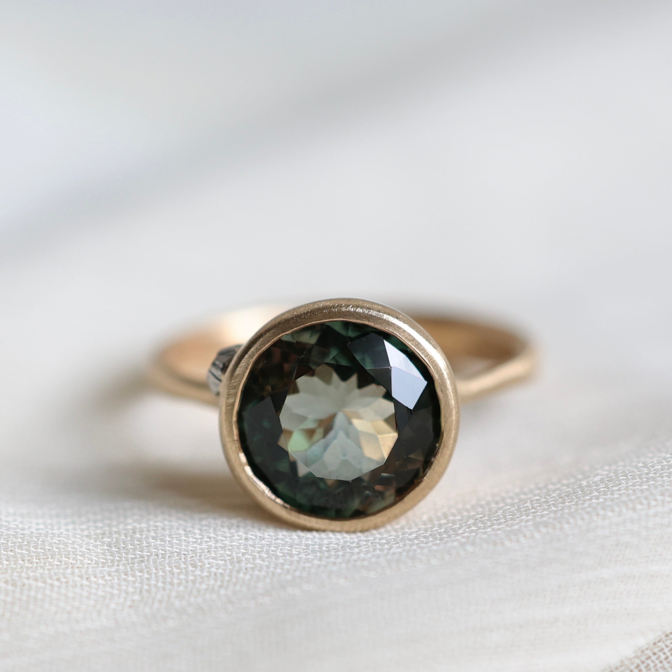 Gold ring with a dark gemstone on a light fabric background