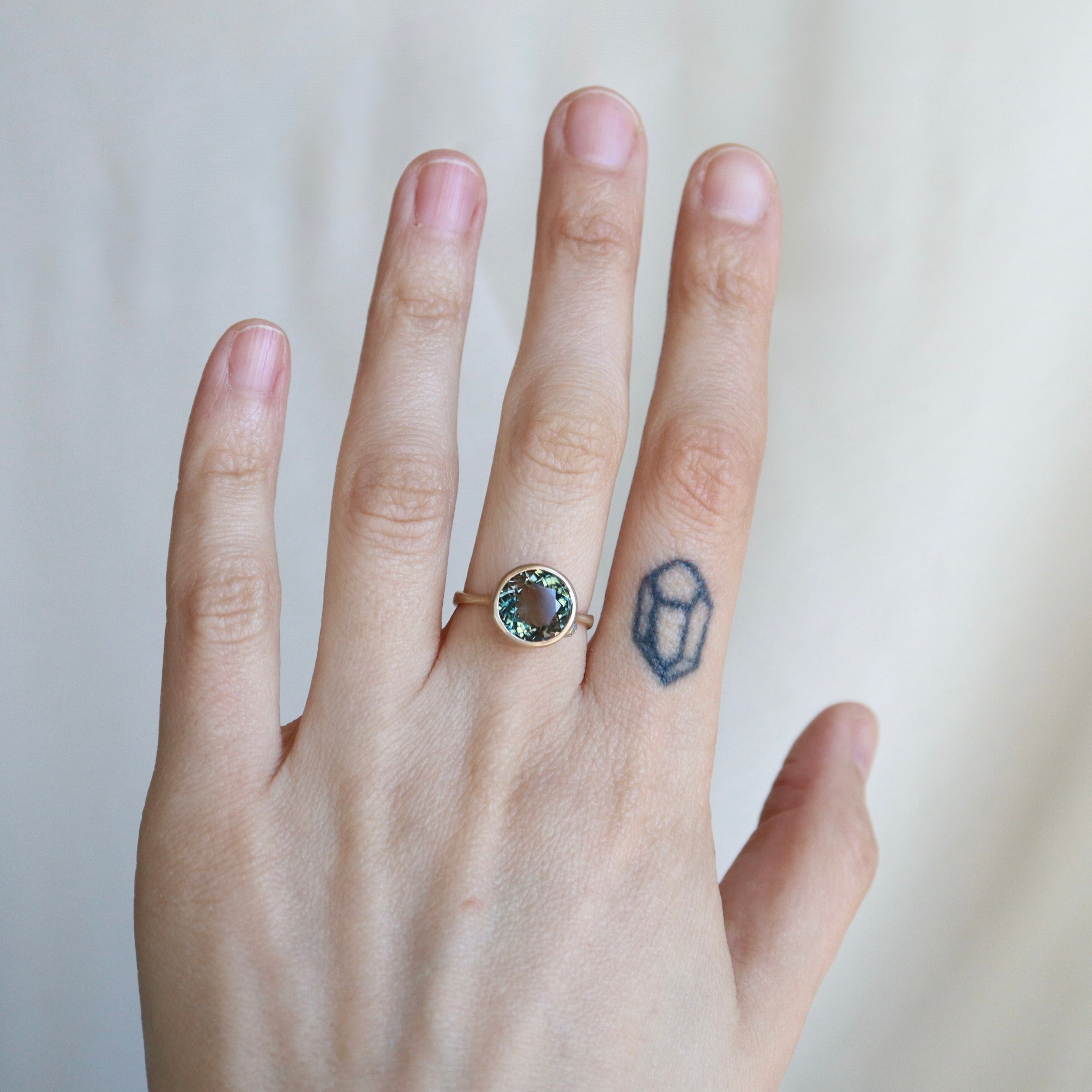 Hand wearing a ring with a gemstone on a plain background