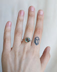 Hand wearing a ring with a gemstone on a plain background
