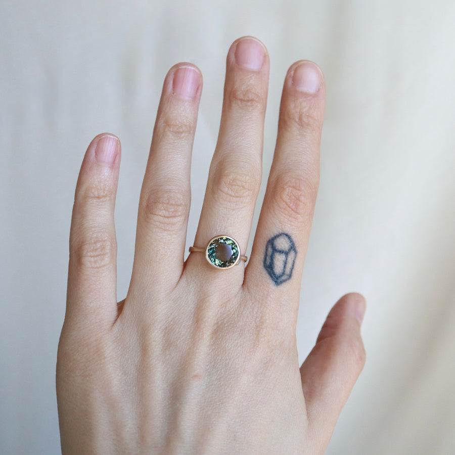 Hand wearing a ring with a gemstone on a plain background