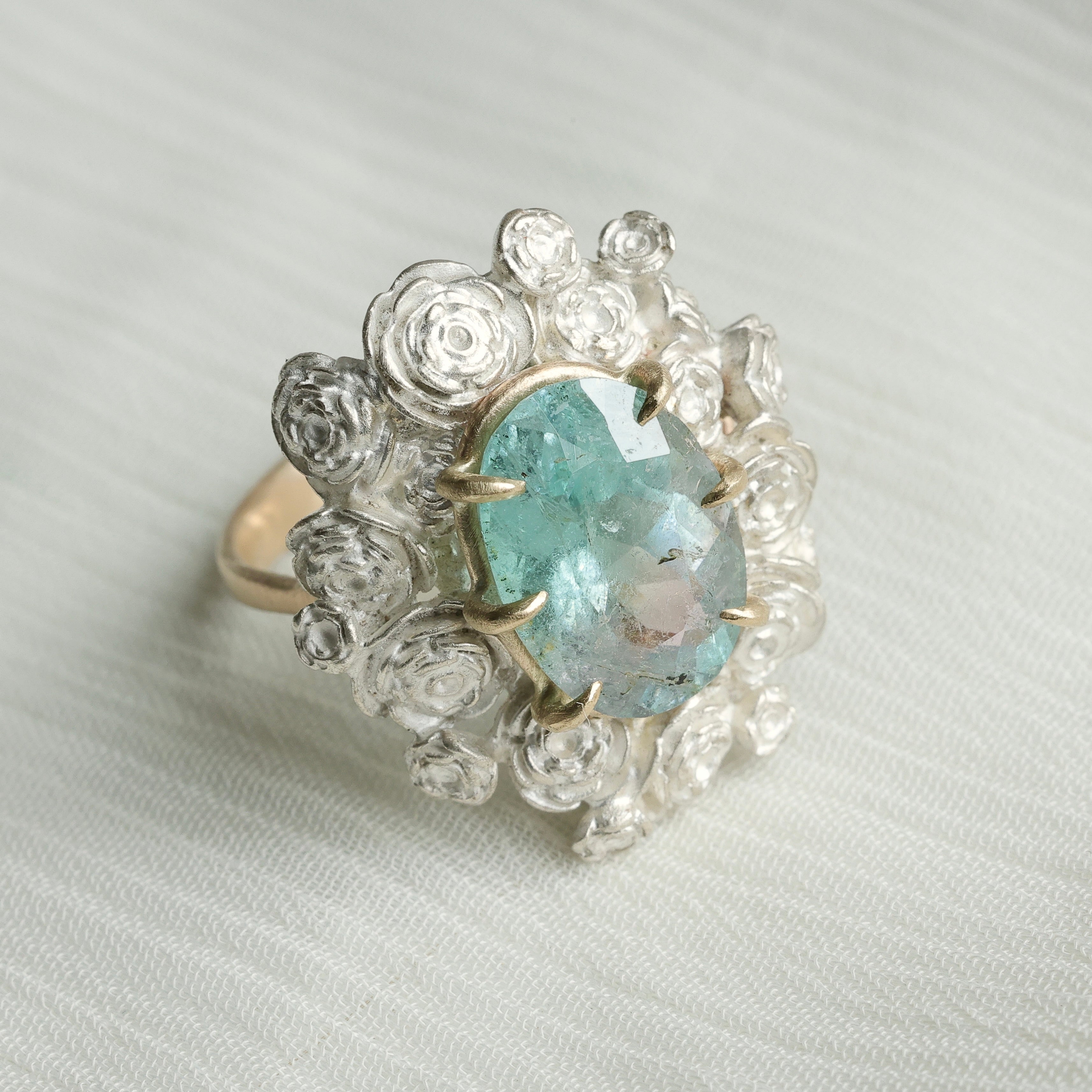 A ring with a wreath of silver roses around a pale blue tourmaline stone