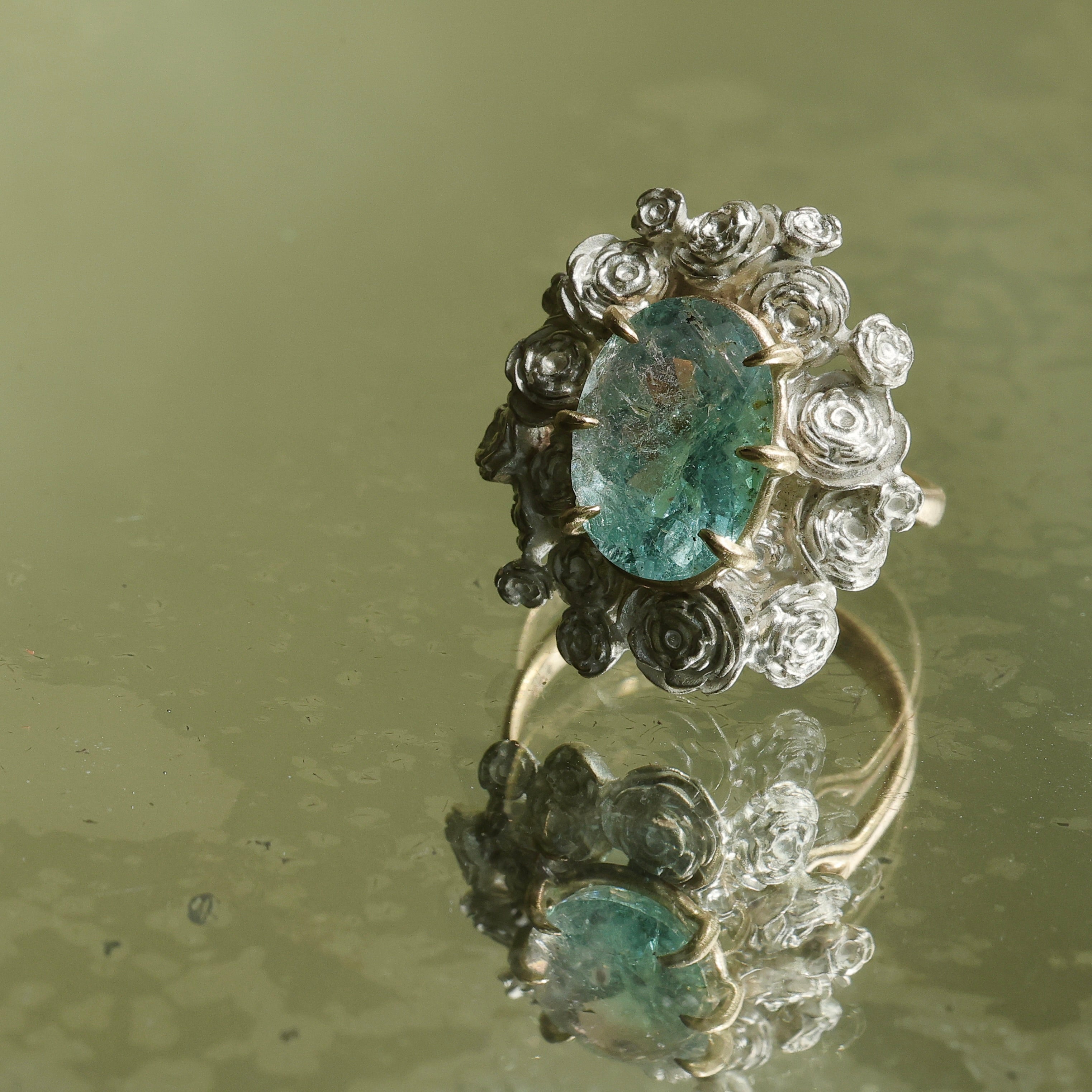 A ring with a wreath of silver roses around a pale blue tourmaline stone
