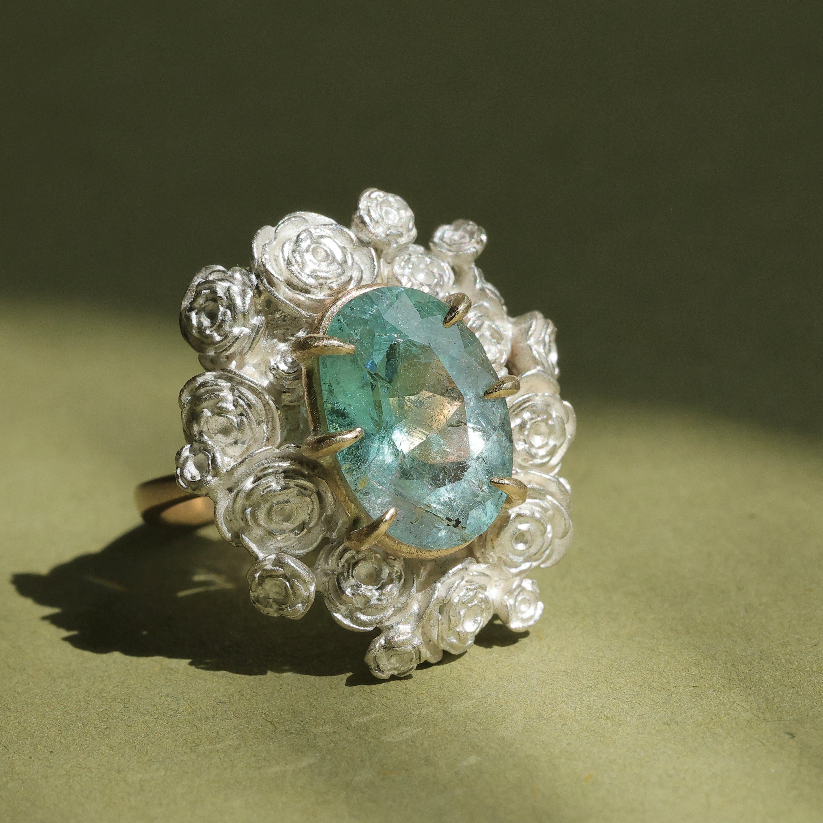 A ring with a wreath of silver roses around a pale blue tourmaline stone