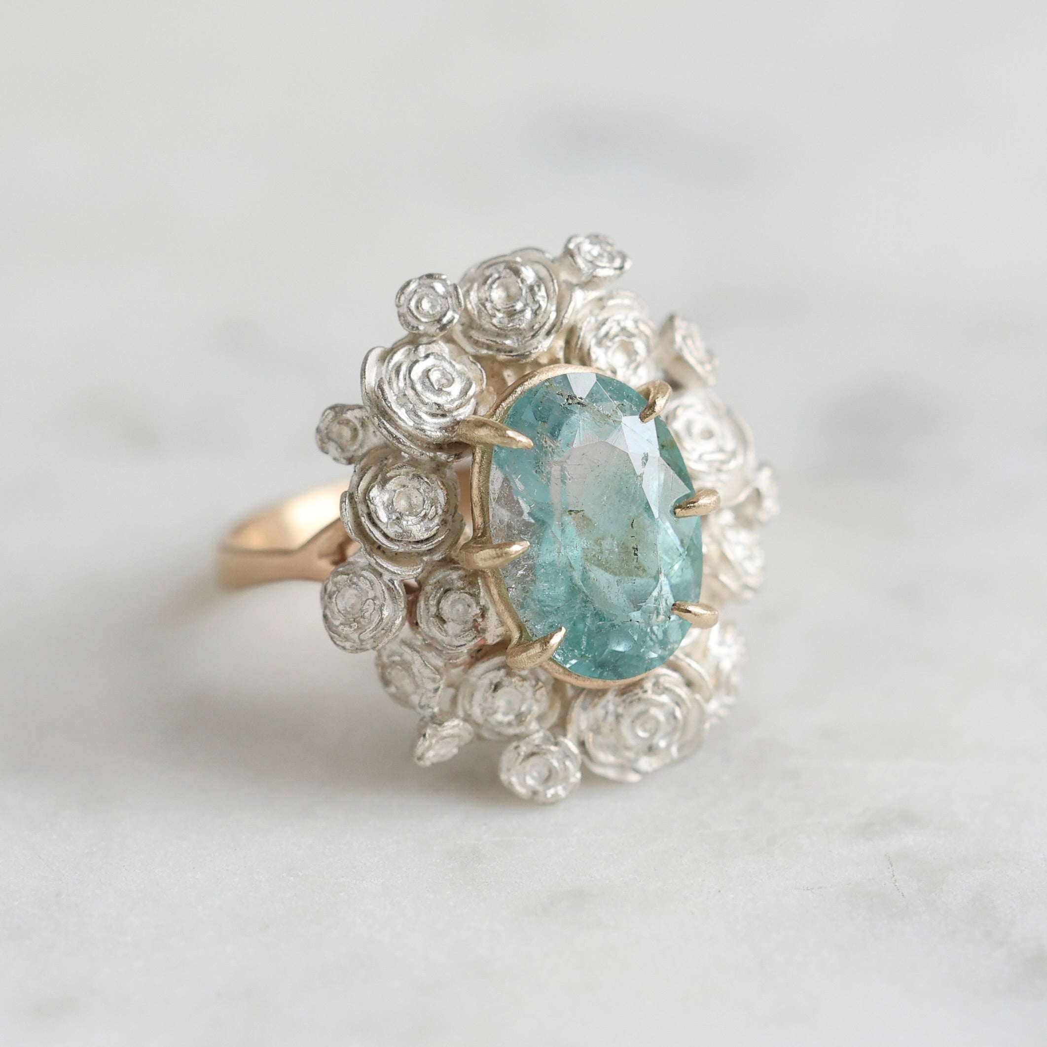 A ring with a wreath of silver roses around a pale blue tourmaline stone