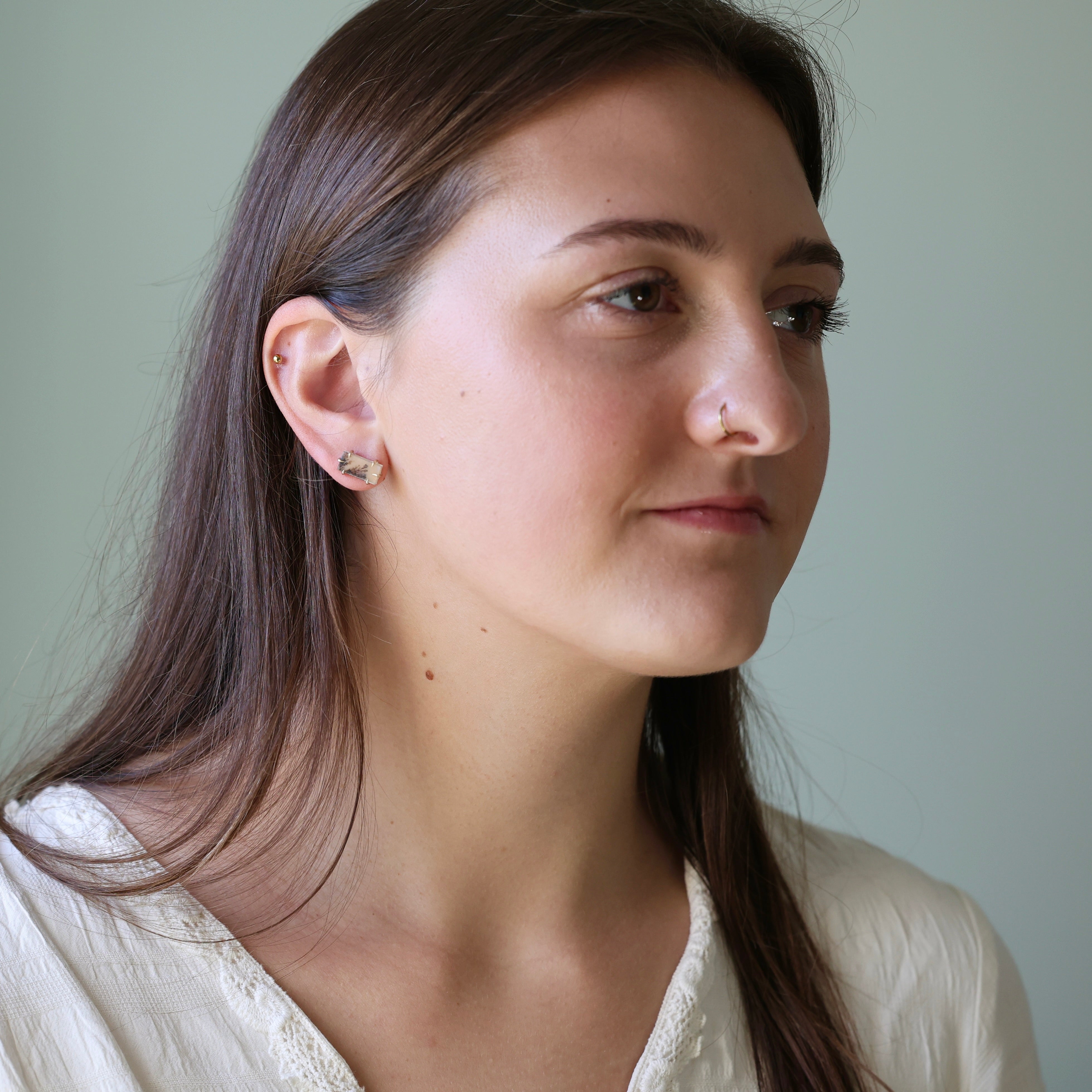 Woman wearing a gold earring against a plain background