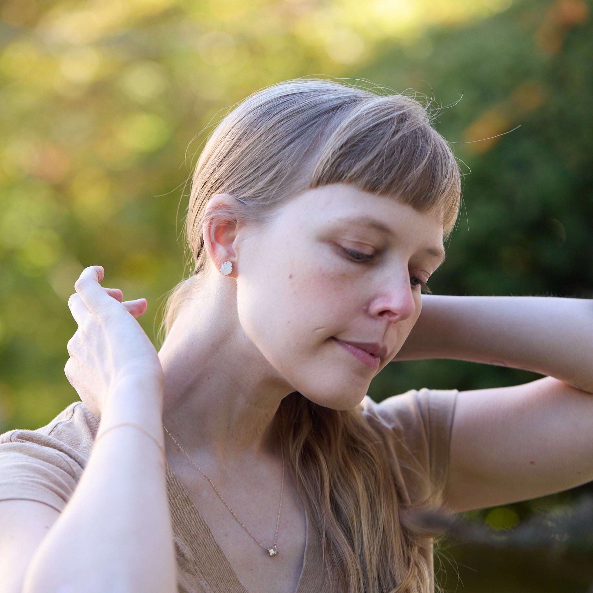 Earring studs: carved moonstone beetles with gold prongs, photographed on person.
