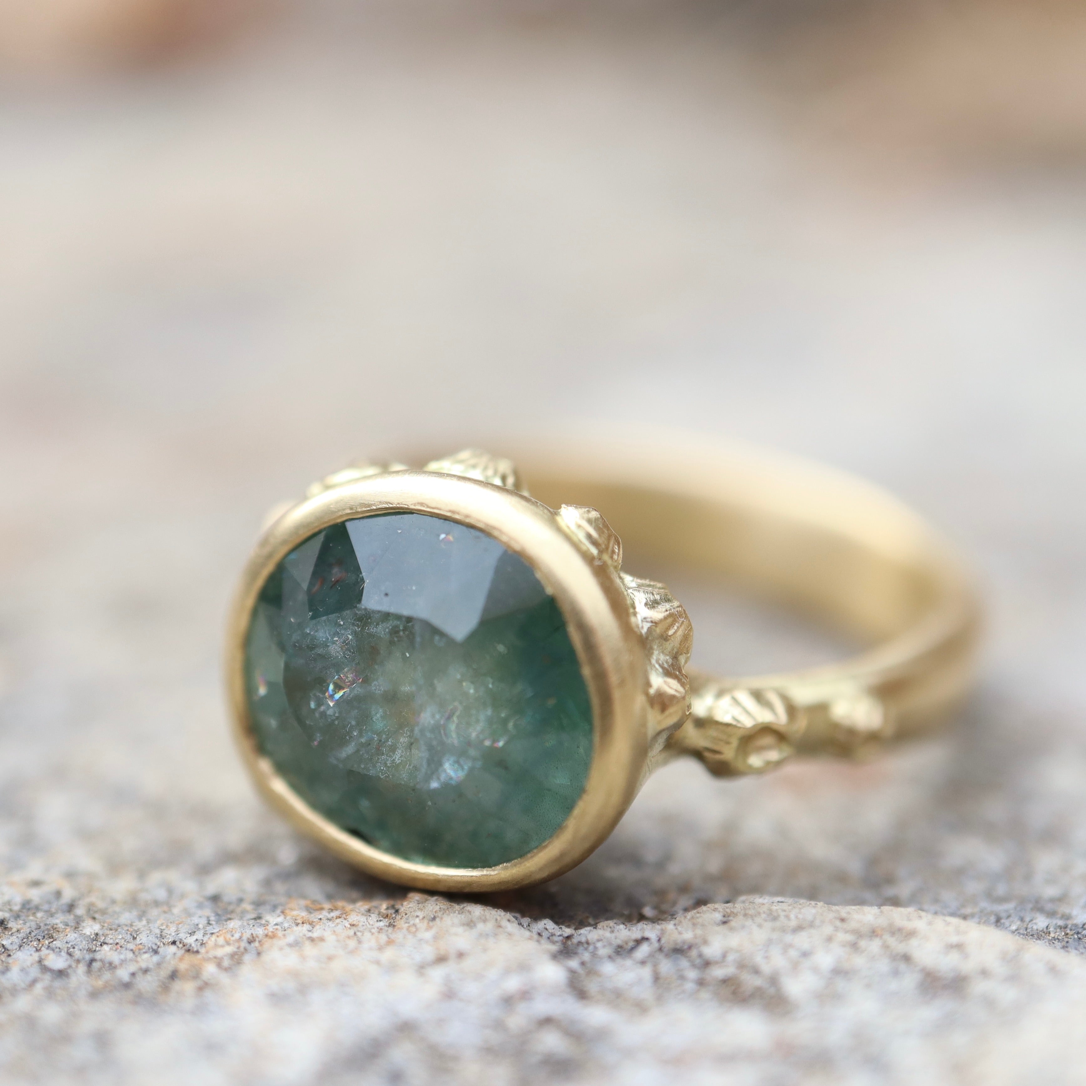 natural light on pale teal montana sapphire set in yellow gold ring with barnacles