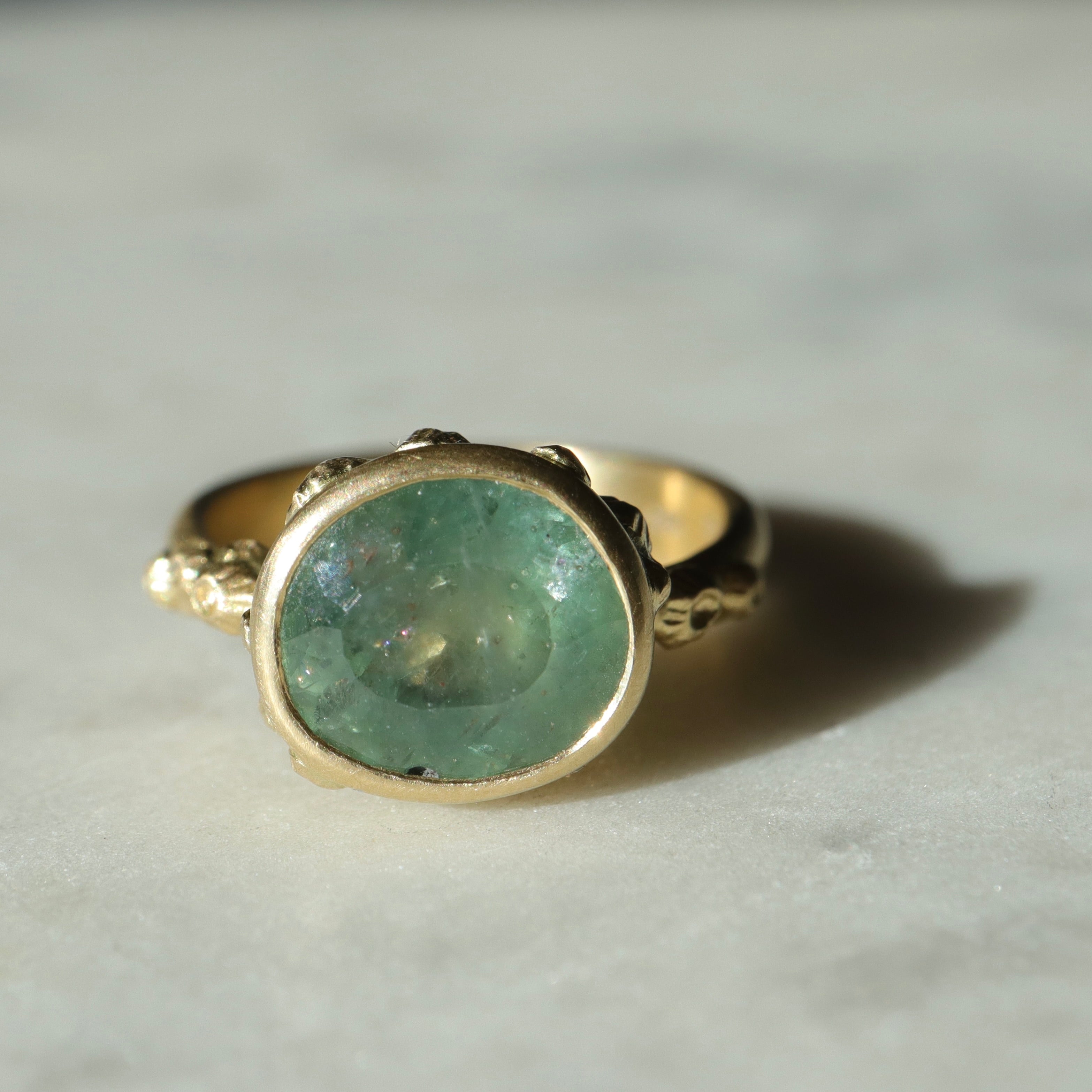 hard natural lighting on a pale teal montana sapphire set in yellow gold ring with barnacles