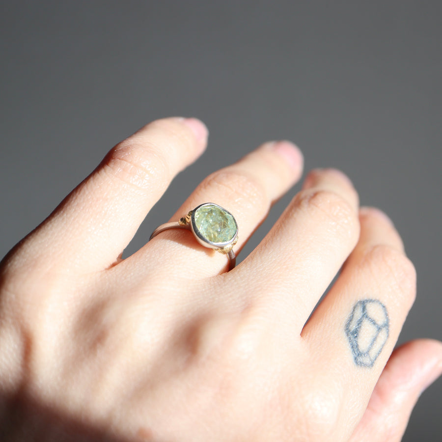 Hand wearing a ring with a green stone on a gray background