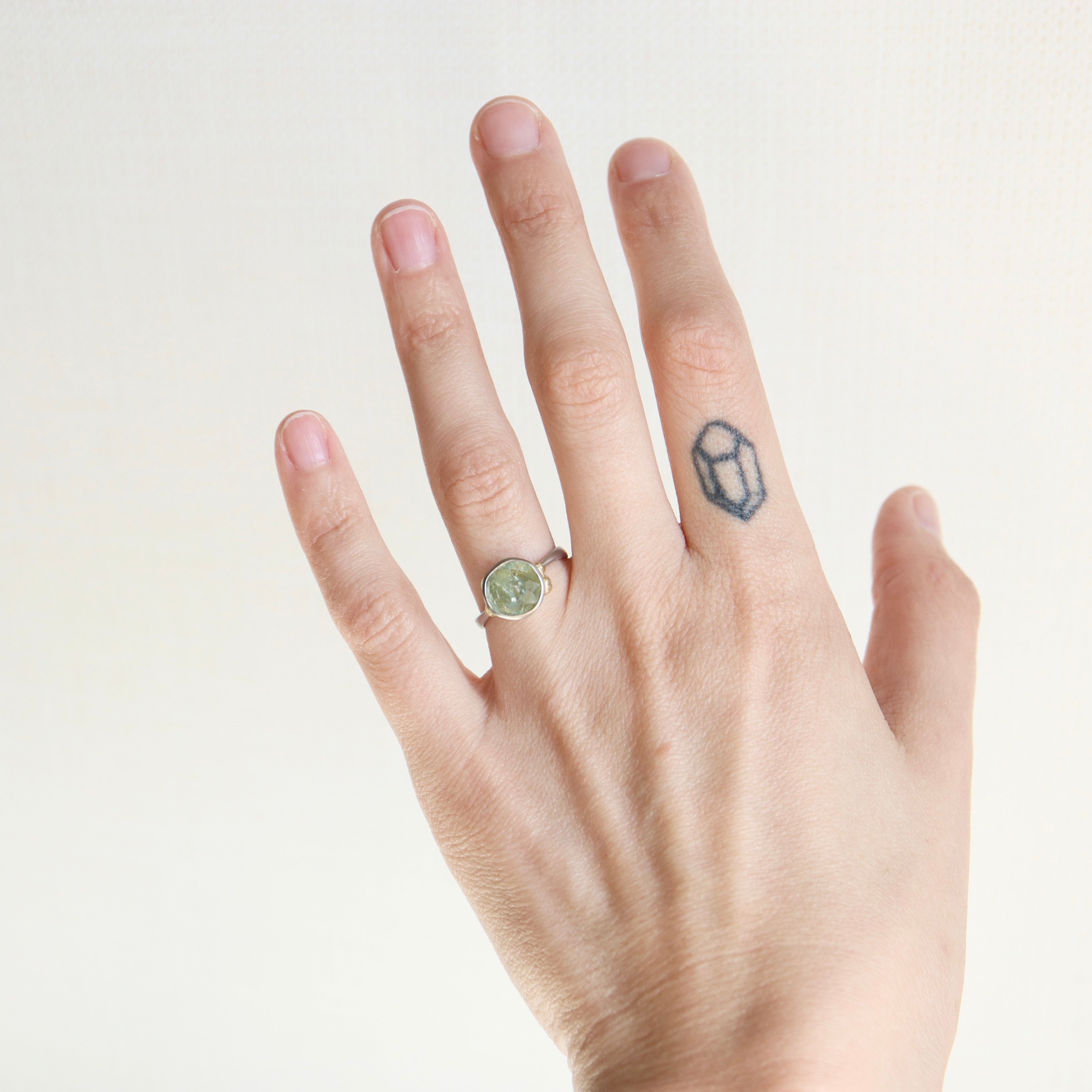 Hand wearing a green gemstone ring on a plain background