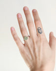 Hand wearing a green gemstone ring on a plain background