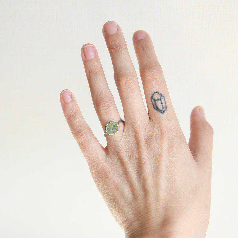 Hand wearing a green gemstone ring on a plain background