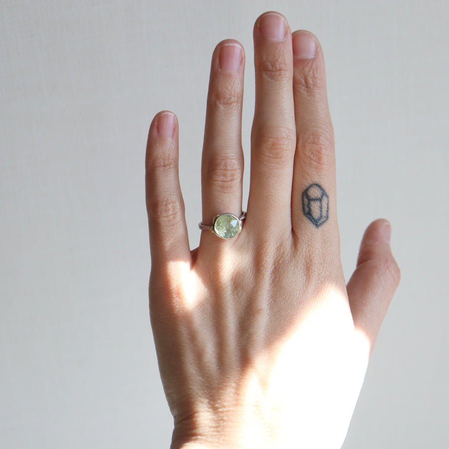 Hand wearing a ring with a green gemstone on a plain background