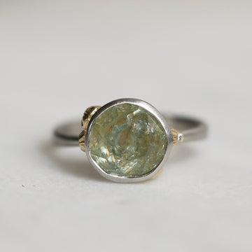 Ring with a green gemstone and platinum band with yellow gold details on a light gray background