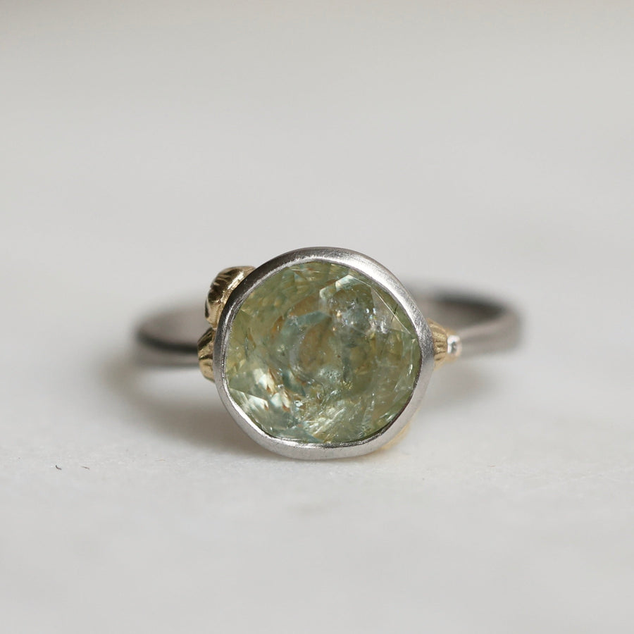 Ring with a green gemstone and platinum band with yellow gold details on a light gray background