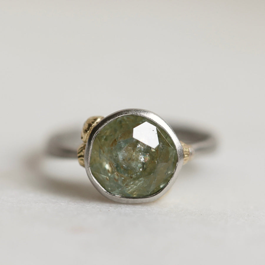 Ring with a green gemstone and platinum band with yellow gold details on a light gray background