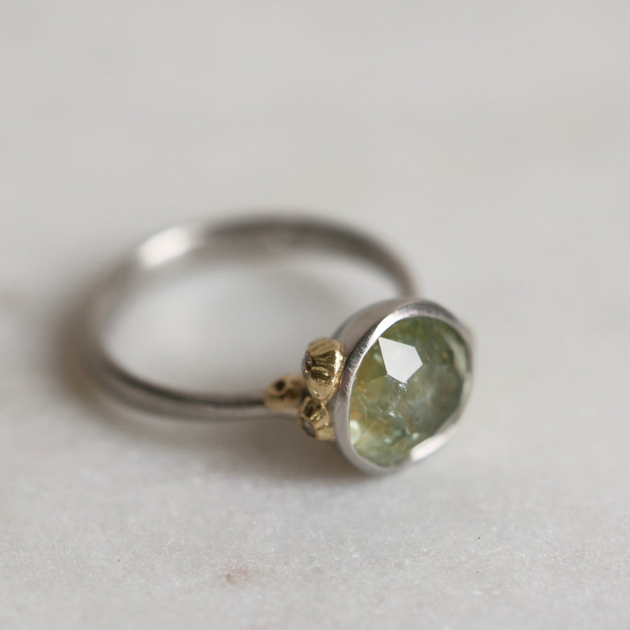 Ring with a green gemstone and platinum band with yellow gold details on a light gray background