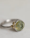 Ring with a green gemstone and platinum band with yellow gold details on a light gray background