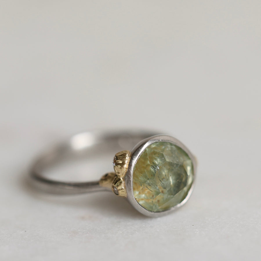 Ring with a green gemstone and platinum band with yellow gold details on a light gray background
