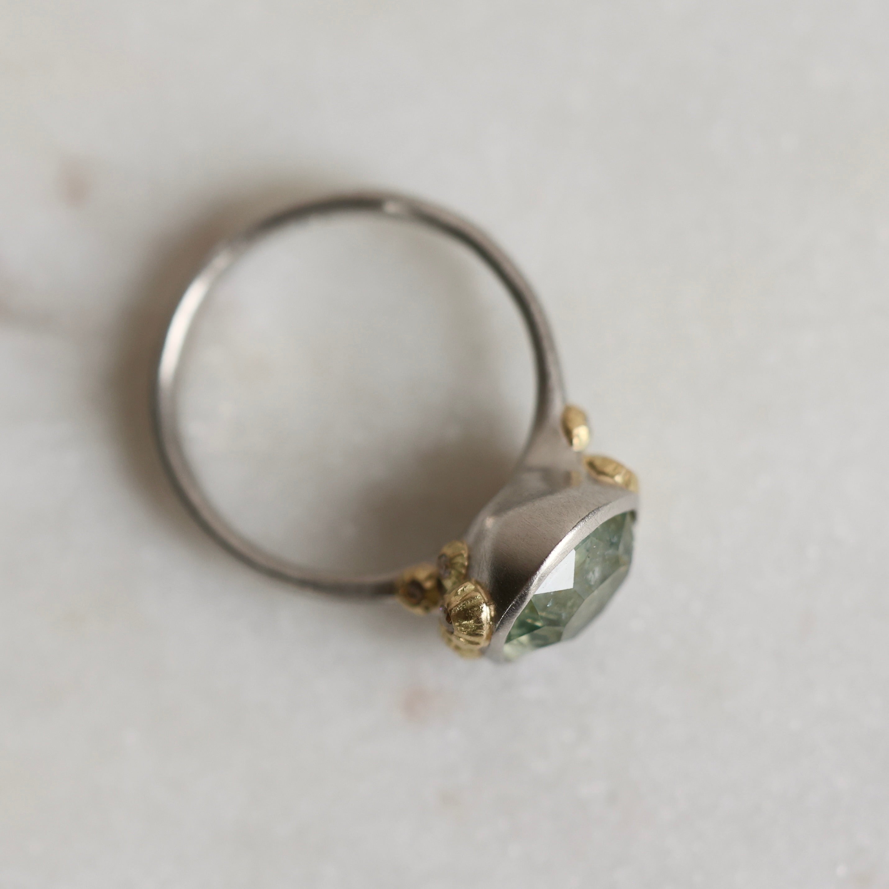 Ring with a green gemstone and platinum band with yellow gold details on a light gray background