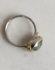 Ring with a green gemstone and platinum band with yellow gold details on a light gray background
