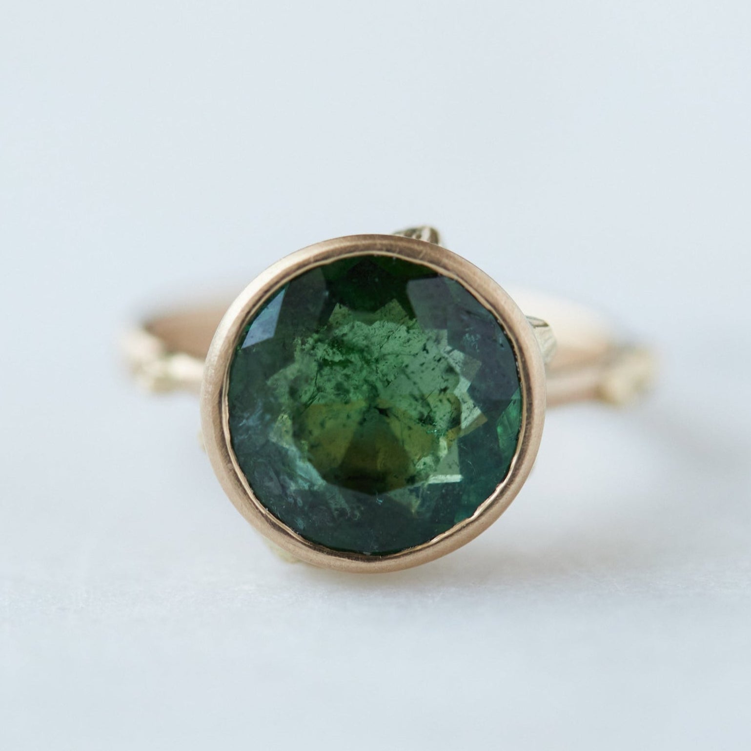 round green faceted tourmaline stone in a gold bezel ring with gold barnacles. Front view.