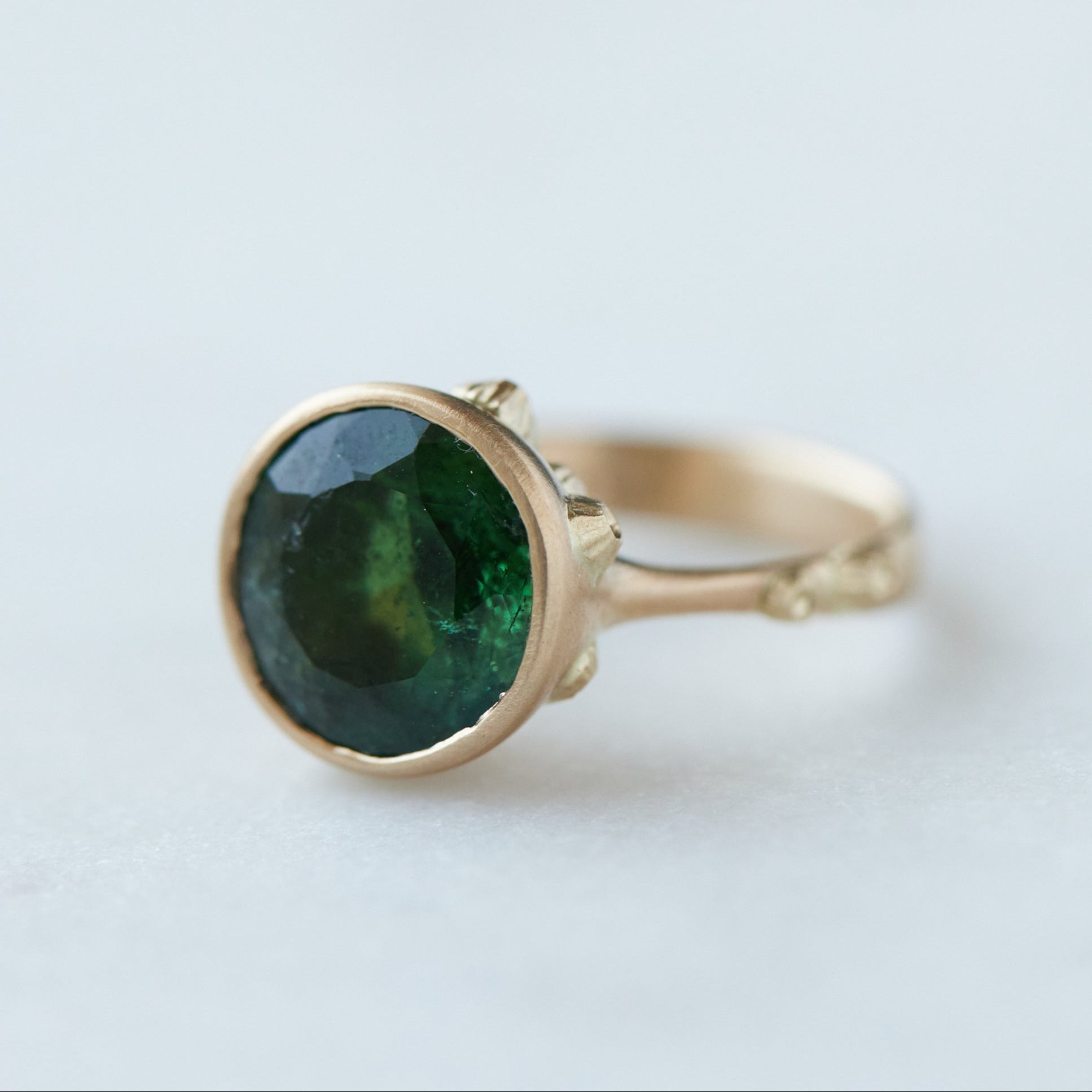 round green faceted tourmaline stone in a gold bezel ring with gold barnacles. 1/4 view.