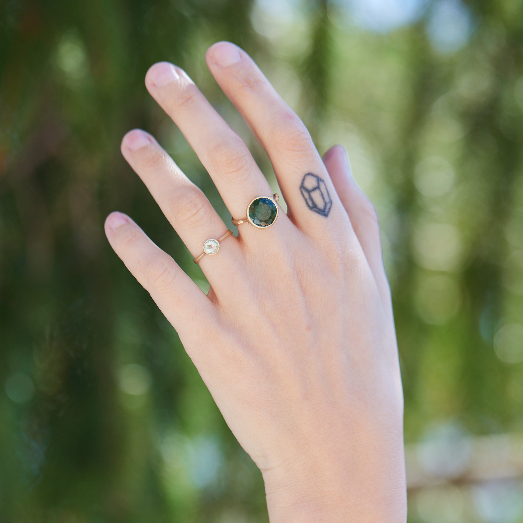 round green faceted tourmaline stone in a gold bezel ring with gold barnacles. Photographed on person.
