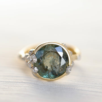 Gold ring with a green gemstone and barnacles on a light background
