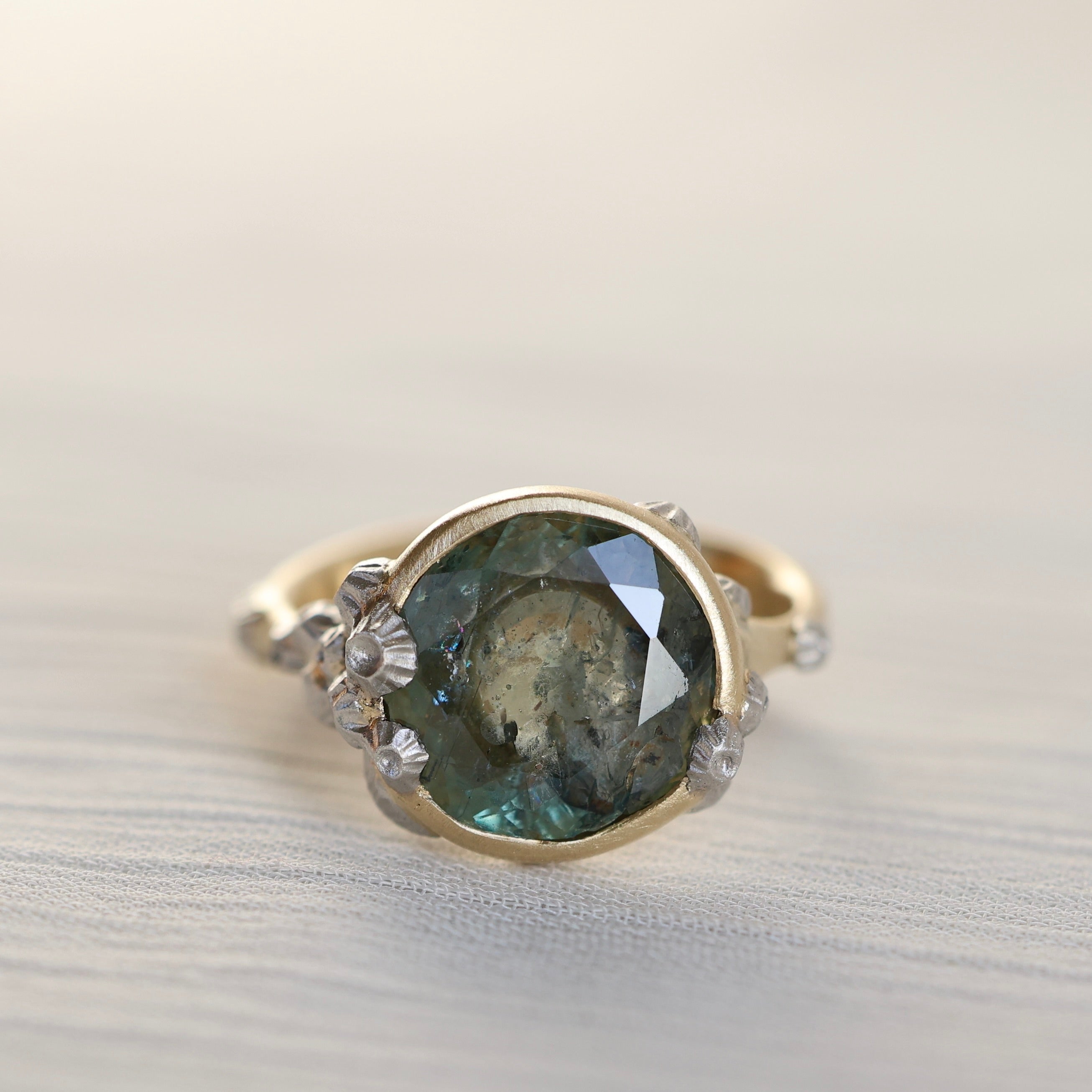 Gold ring with a green gemstone and barnacles on a light background