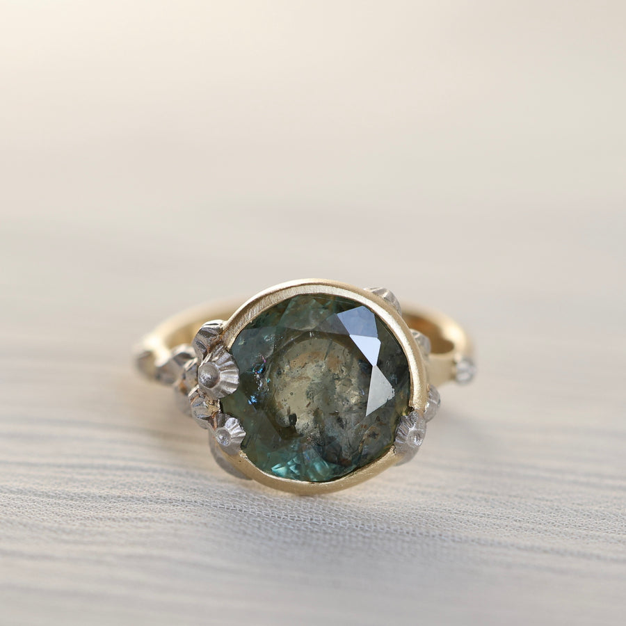 Gold ring with a green gemstone and barnacles on a light background