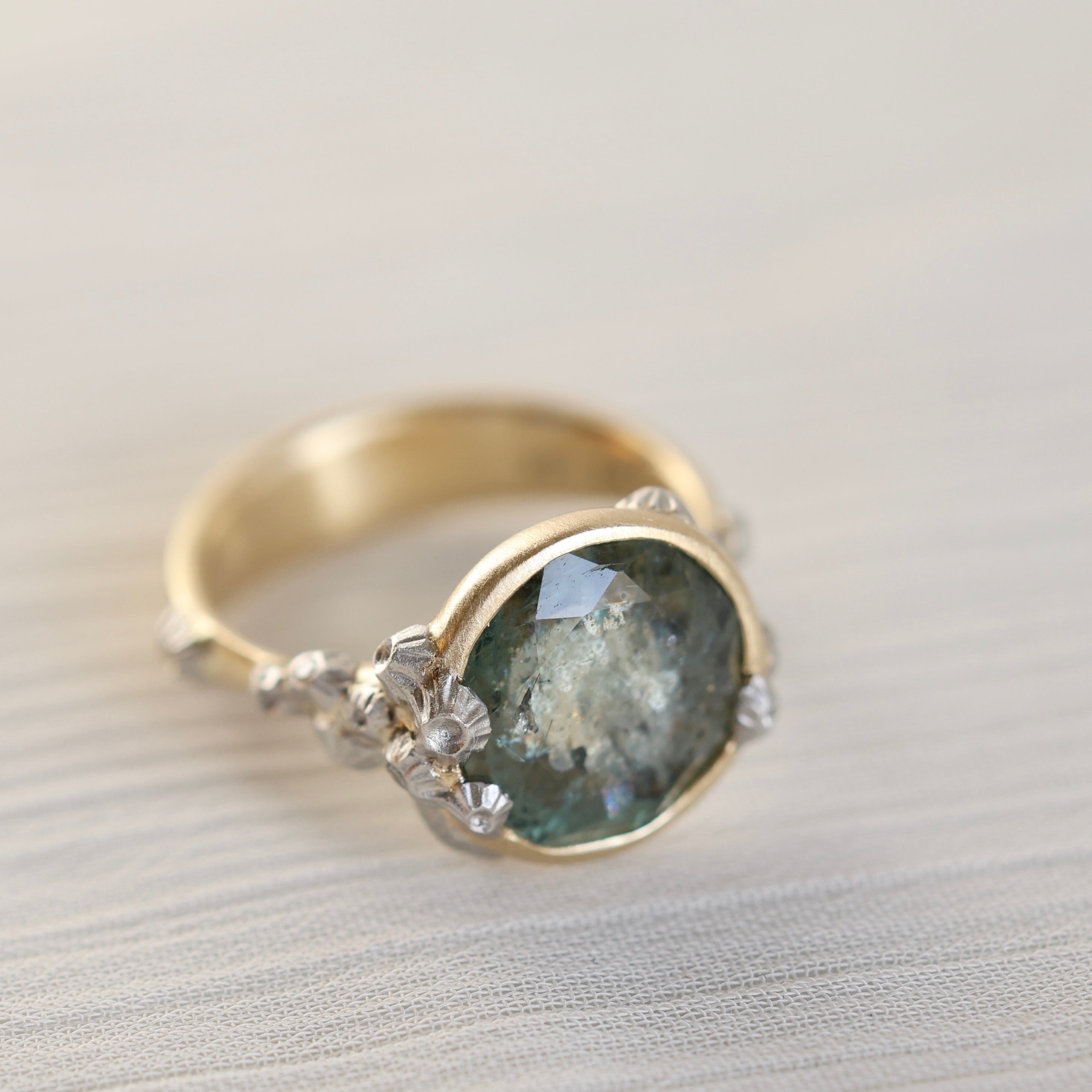 Gold ring with a green gemstone and barnacles on a light background