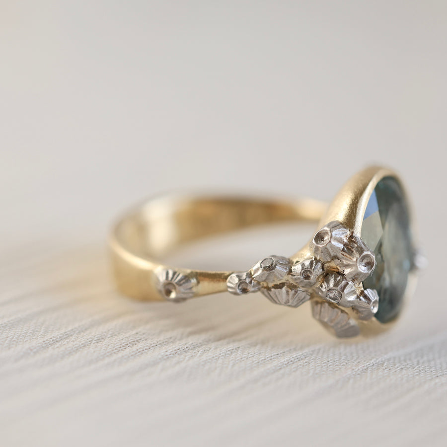 Gold ring with a green gemstone and barnacles on a light background