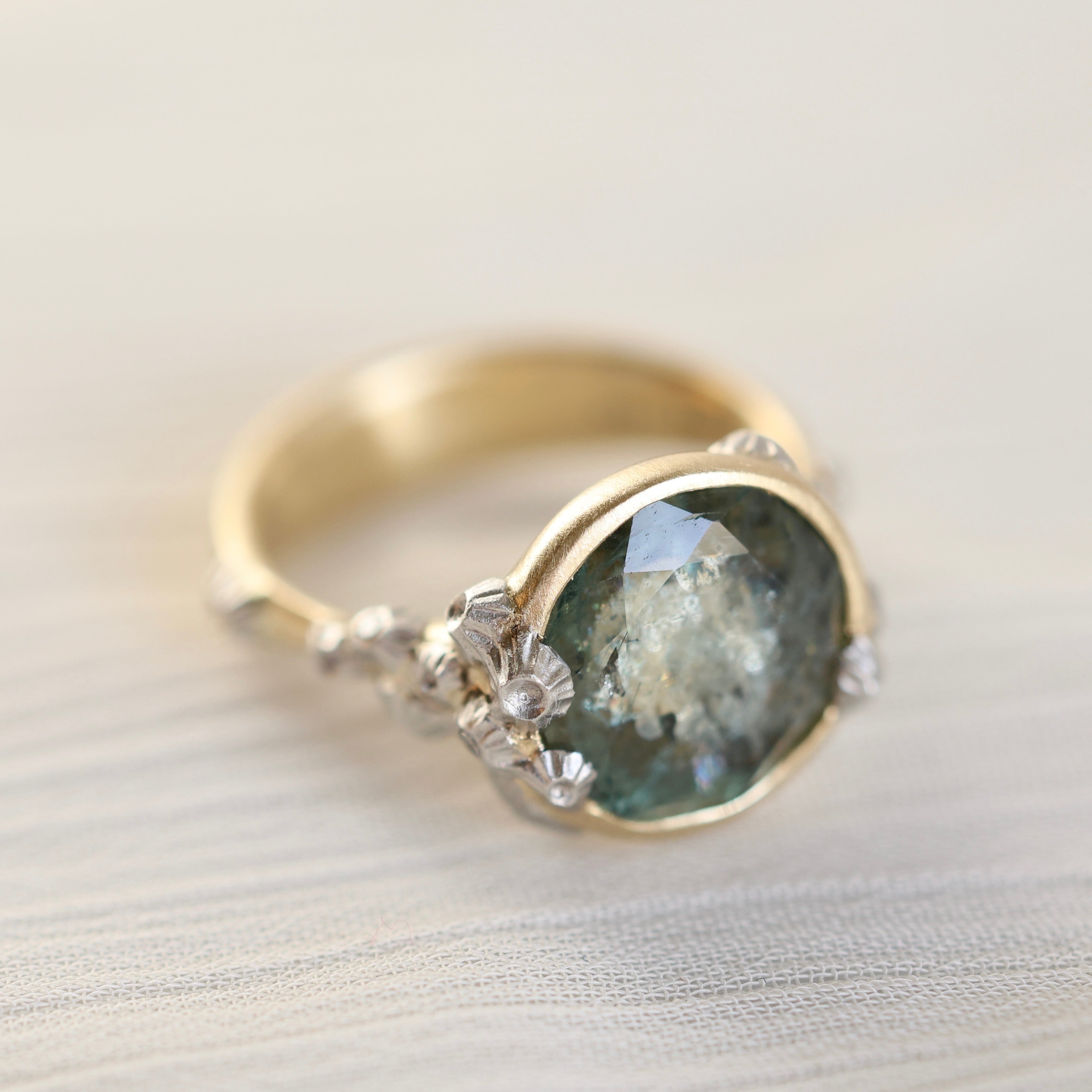 Gold ring with a green gemstone and barnacles on a light background