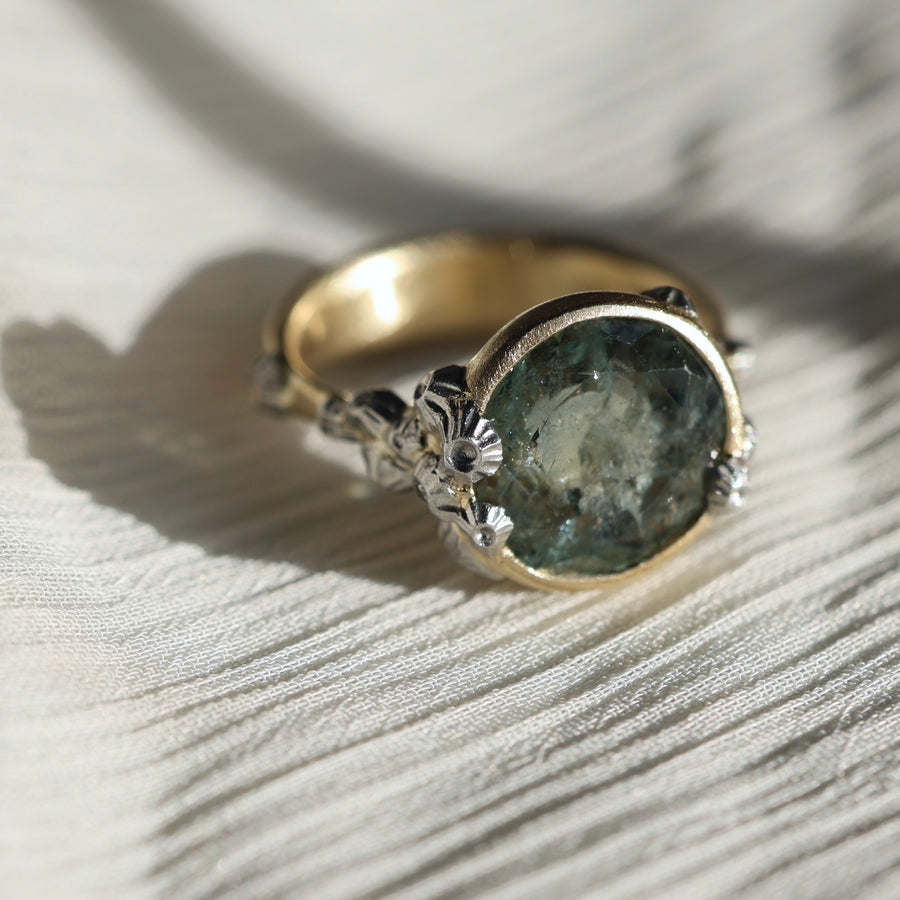 Gold ring with a green gemstone and barnacles on a light background